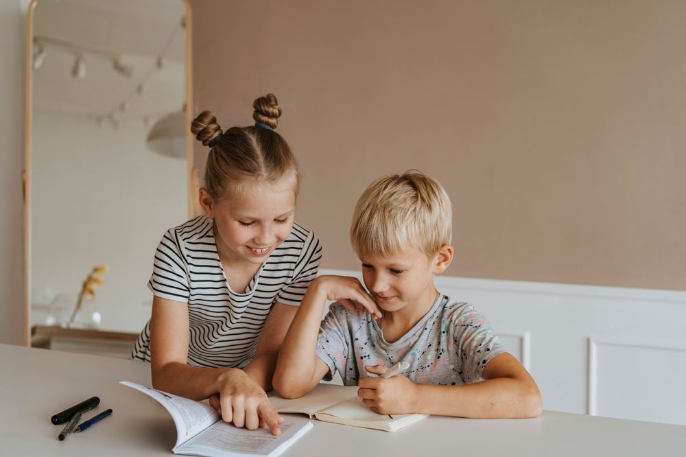 Two children learning together at a table with books